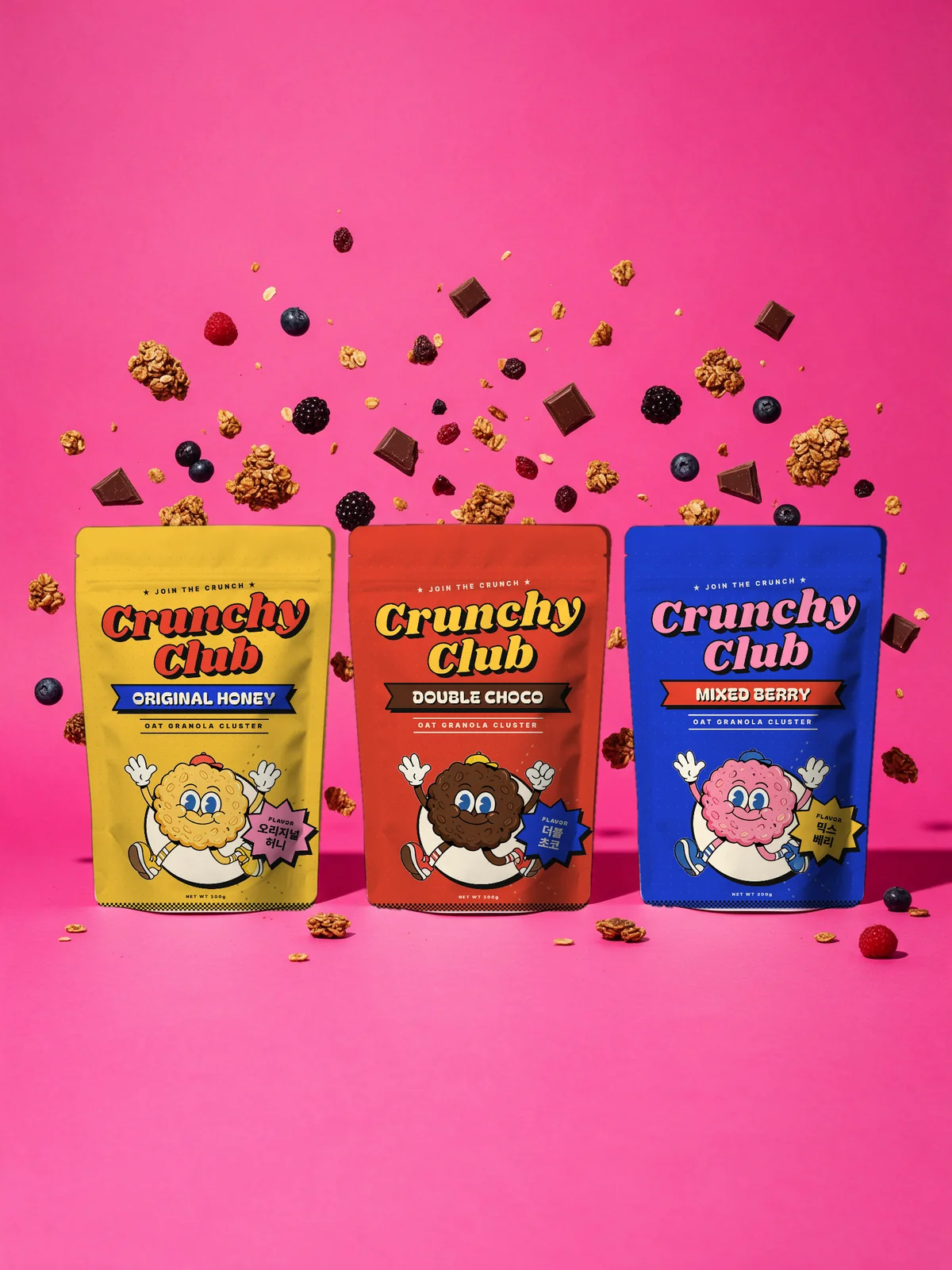 Three Crunchy Club pouches, yellow, red and blue, on a hot pink backdrop with floating granola, chocolate and berries